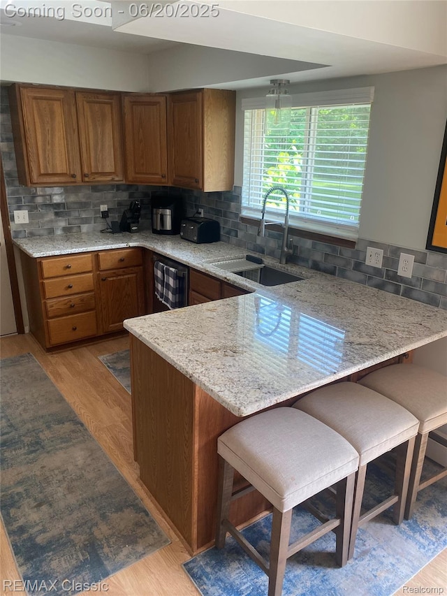 3417 Ramada Dr, Highland, MI 48356 - kitchen with a peninsula, brown cabinetry, backsplash, light wood-style flooring, and a breakfast bar