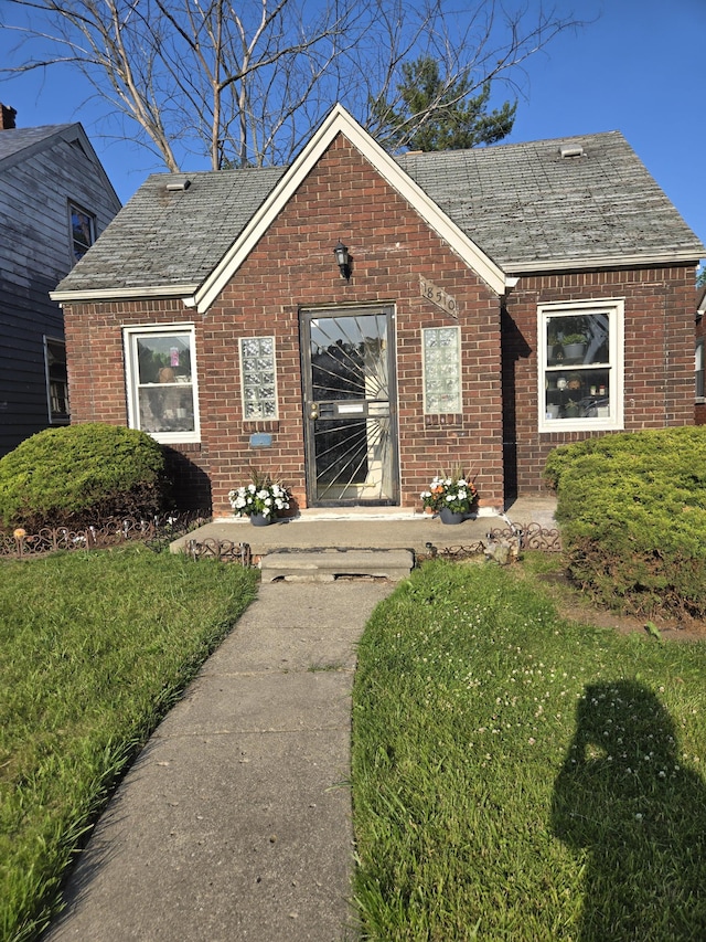 18510 Alcoy Ave, Detroit, MI 48205 - view of front of house with brick siding, a front lawn, and a shingled roof