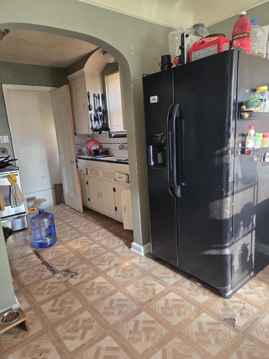 18510 Alcoy Ave, Detroit, MI 48205 - kitchen featuring black fridge, arched walkways, stainless steel stove, white cabinetry, and backsplash