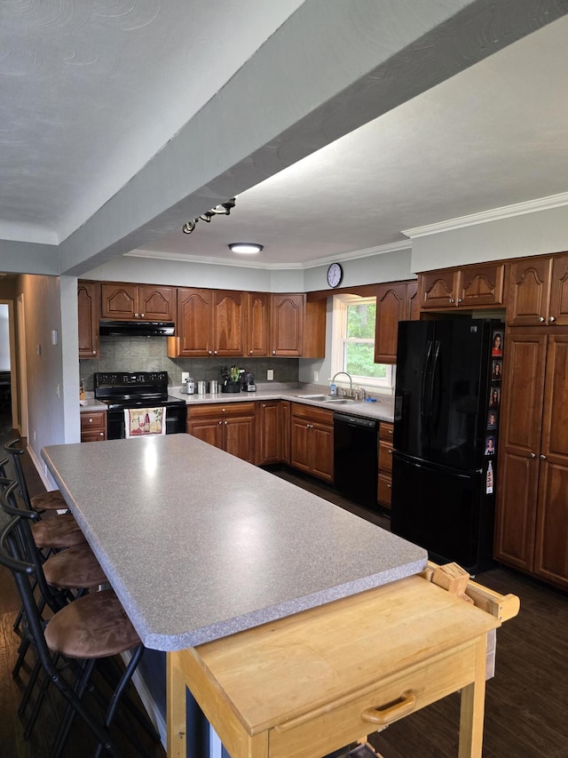 28548 Fairlane Dr, Dowagiac, MI 49047 - kitchen featuring black appliances, under cabinet range hood, dark wood-style floors, ornamental molding, and a kitchen island