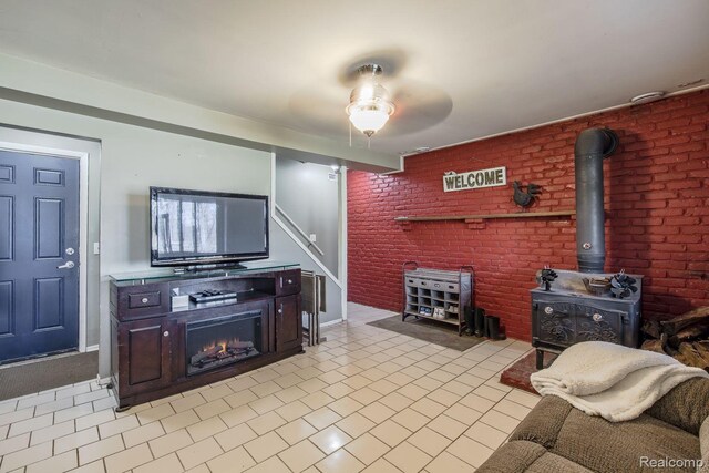 12109 Shaffer Rd, Davisburg, MI 48350 - living room featuring a wood stove, stairs, a ceiling fan, light tile patterned flooring, and brick wall