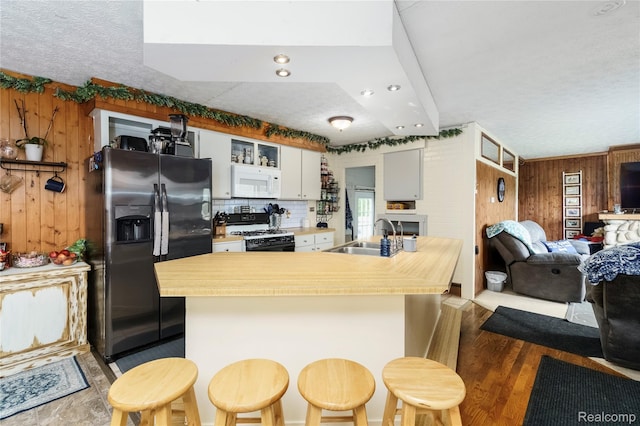 5045 Baldwin Rd, Swartz Creek, MI 48473 - kitchen featuring black gas stove, fridge with ice dispenser, white microwave, wooden walls, and white cabinets