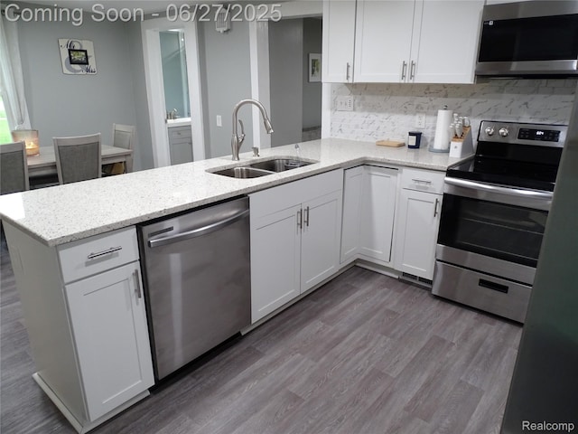11306 W St, Grand Blanc, MI 48439 - kitchen with appliances with stainless steel finishes, a peninsula, white cabinetry, decorative backsplash, and light stone counters