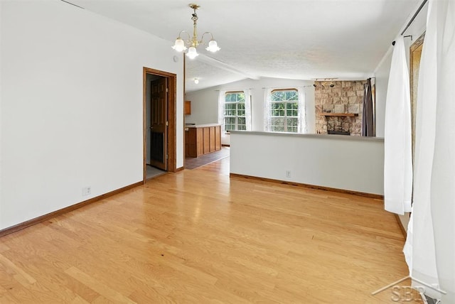 3227 S 11 Mile Rd, Auburn, MI 48611 - spare room featuring a chandelier, light wood-type flooring, lofted ceiling, and a stone fireplace