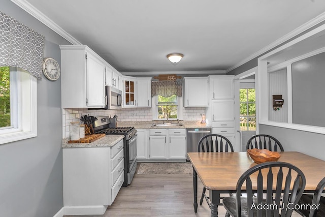 3655 Giddings Ave SE, Grand Rapids, MI 49508 - kitchen featuring appliances with stainless steel finishes, white cabinetry, decorative backsplash, light wood-style floors, and crown molding