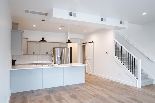 2458 Maes Rd, West Branch, MI 48661 - kitchen featuring stainless steel refrigerator with ice dispenser, gray cabinetry, a barn door, light wood finished floors, and a peninsula
