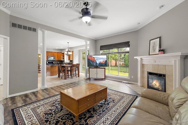 18852 Newbridge Dr, Macomb, MI 48044 - living room featuring decorative columns, ceiling fan, light wood-style flooring, a tiled fireplace, and crown molding