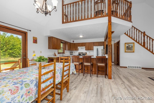 8651 22 Mile Rd NE, Sand Lake, MI 49343 - dining area featuring high vaulted ceiling, light wood-style floors, stairs, and a chandelier
