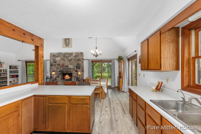 8651 22 Mile Rd NE, Sand Lake, MI 49343 - kitchen featuring lofted ceiling, brown cabinetry, light wood-type flooring, light countertops, and a stone fireplace