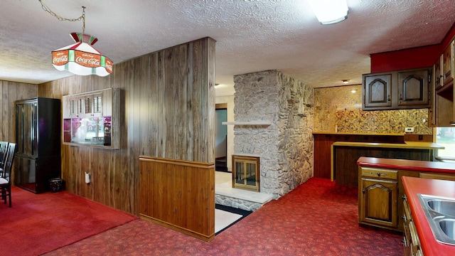 5724 E Townline Rd, Birch Run, MI 48415 - kitchen with carpet floors, a textured ceiling, freestanding refrigerator, wooden walls, and a stone fireplace
