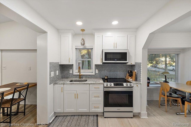 2231 N St, Milford, MI 48380 - kitchen featuring white microwave, stainless steel electric range oven, light wood-style flooring, white cabinetry, and decorative backsplash