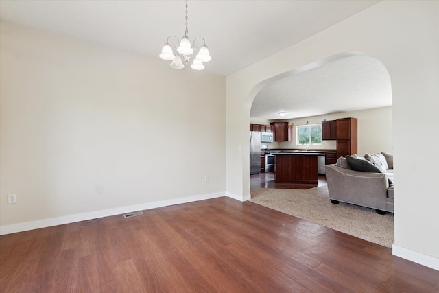 14704 Crescent Meadows Dr, Cedar Springs, MI 49319 - unfurnished living room with arched walkways, dark wood-style floors, and a chandelier