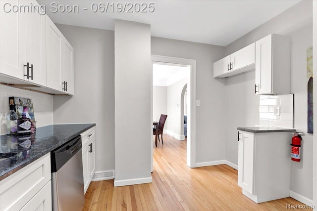 243 2nd St, Brownstown, MI 48192 - kitchen featuring dishwasher, light wood-type flooring, arched walkways, white cabinetry, and dark stone countertops
