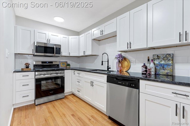 243 2nd St, Brownstown, MI 48192 - kitchen with appliances with stainless steel finishes, decorative backsplash, light wood finished floors, dark stone counters, and white cabinets