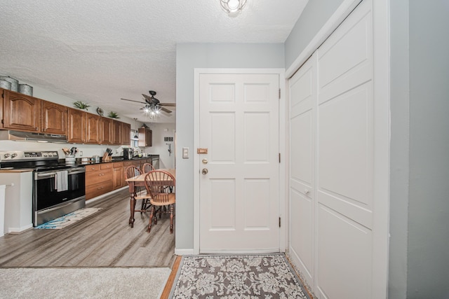 1361 Holmes Rd, Ypsilanti, MI 48198 - kitchen with stainless steel electric range, under cabinet range hood, a textured ceiling, ceiling fan, and brown cabinets