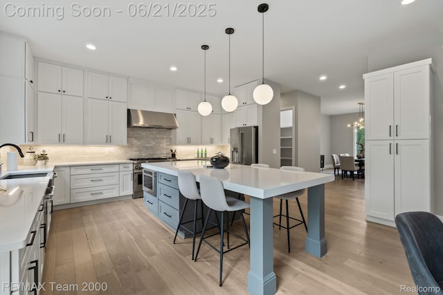 32575 Romsey Rd, Franklin, MI 48025 - kitchen featuring wall chimney range hood, appliances with stainless steel finishes, light wood-type flooring, white cabinets, and recessed lighting