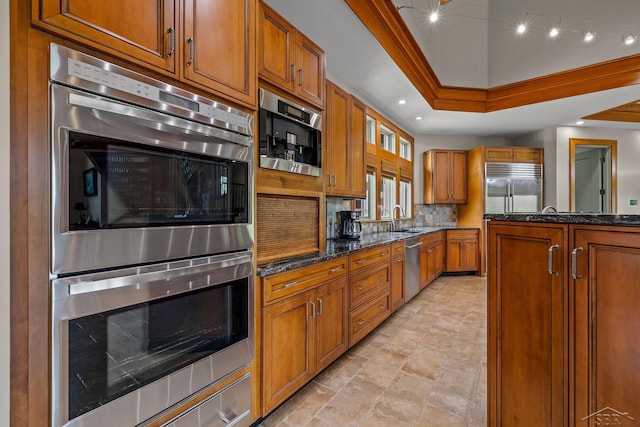 199 E Brooks Rd, Midland, MI 48640 - kitchen featuring appliances with stainless steel finishes, brown cabinetry, dark stone countertops, decorative backsplash, and a raised ceiling