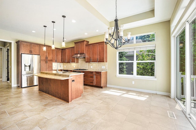 8842 Oakland Hills Cir, Portage, MI 49024 - kitchen with stainless steel refrigerator with ice dispenser, under cabinet range hood, a chandelier, decorative backsplash, and brown cabinetry