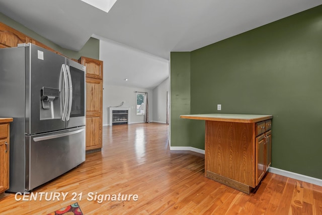2364 Milford Dr, Saginaw, MI 48603 - kitchen featuring stainless steel refrigerator with ice dispenser, light wood-style flooring, brown cabinetry, lofted ceiling, and a fireplace