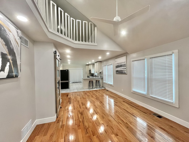 336 E Prospect St, Jackson, MI 49203 - unfurnished living room with a barn door, light wood-style floors, recessed lighting, high vaulted ceiling, and a ceiling fan