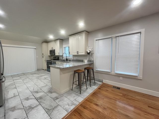 336 E Prospect St, Jackson, MI 49203 - kitchen featuring appliances with stainless steel finishes, a kitchen bar, recessed lighting, white cabinetry, and a peninsula