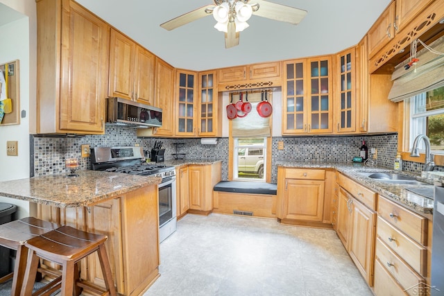 8603 Millington Rd, Vassar, MI 48768 - kitchen with appliances with stainless steel finishes, ceiling fan, light stone countertops, a breakfast bar area, and glass insert cabinets