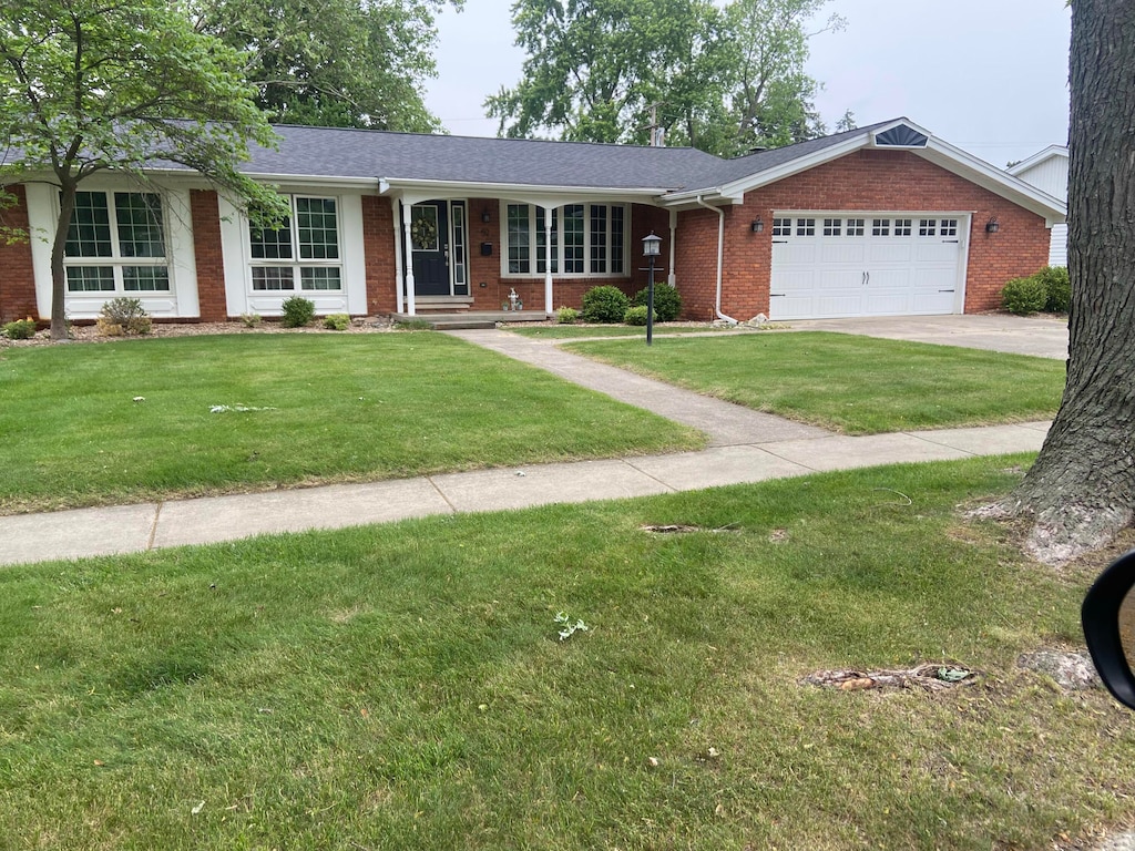 52 W Miller Ave, Milan, MI 48160 - ranch-style house with brick siding, an attached garage, a front yard, concrete driveway, and a shingled roof
