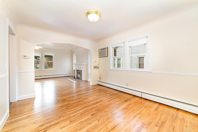 395 S Center Rd, Saginaw, MI 48638 - spare room featuring a baseboard heating unit, a fireplace, arched walkways, and light wood-type flooring