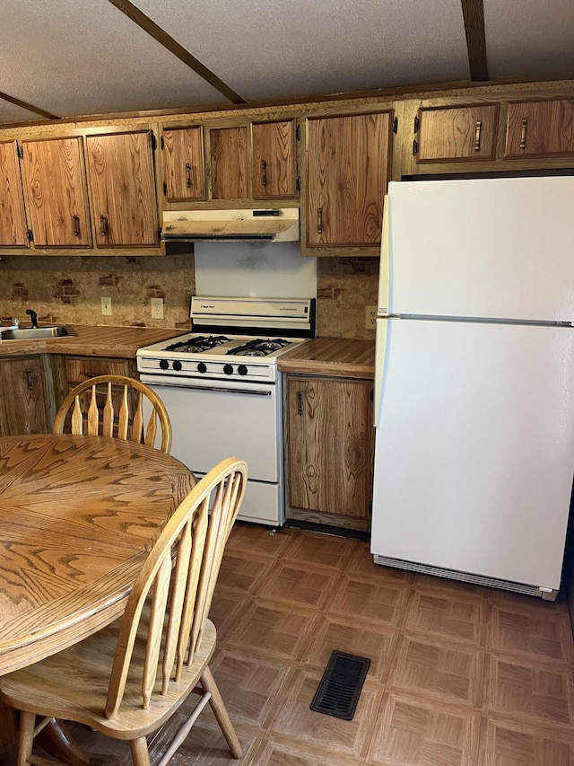 6121 N Pine Ave, White Cloud, MI 49349 - kitchen featuring white appliances, under cabinet range hood, brown cabinets, and decorative backsplash