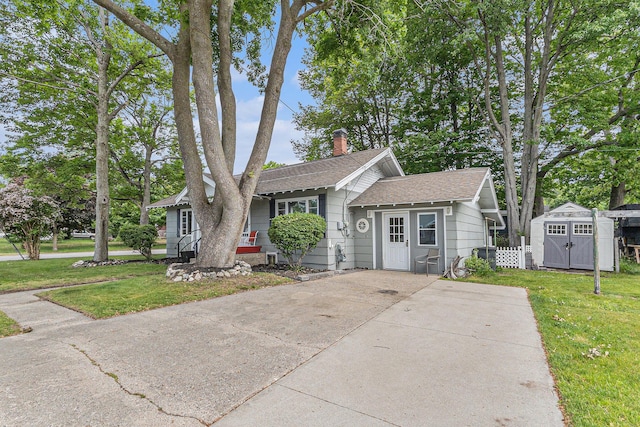 101 E Whittier St, Ludington, MI 49431 - view of front of home featuring a shed, a chimney, a front yard, roof with shingles, and driveway