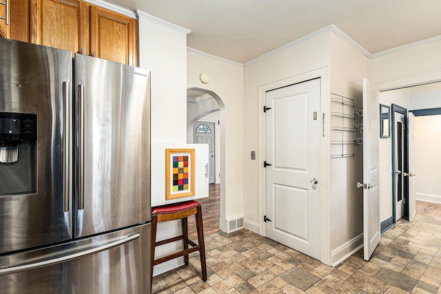 101 E Whittier St, Ludington, MI 49431 - kitchen featuring stainless steel fridge with ice dispenser, stone finish floors, brown cabinets, arched walkways, and ornamental molding