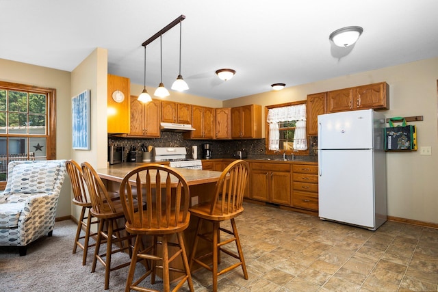 1724 N Ridge Rd, Mears, MI 49436 - kitchen with white appliances, under cabinet range hood, brown cabinets, backsplash, and a peninsula