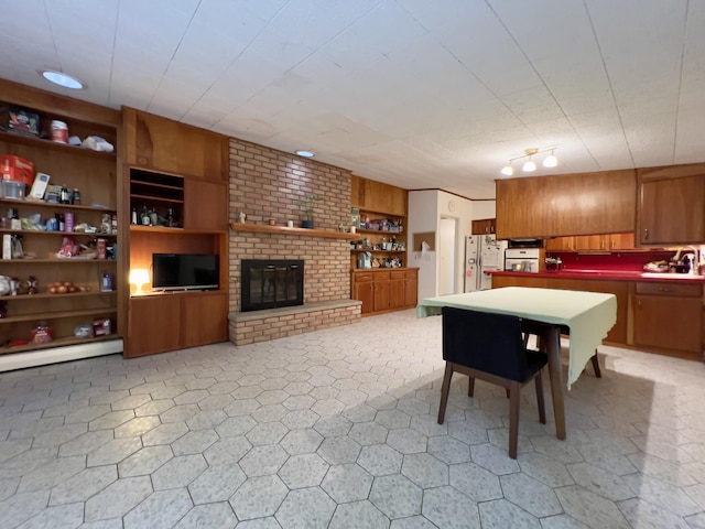 3431 Pineview Dr, Dexter, MI 48130 - kitchen with freestanding refrigerator, brown cabinets, open shelves, a brick fireplace, and a baseboard radiator