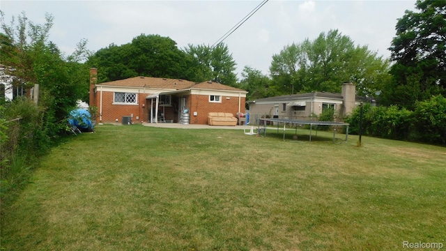 27038 Grobbel Dr, Warren, MI 48092 - back of house with a trampoline, a yard, brick siding, and a chimney