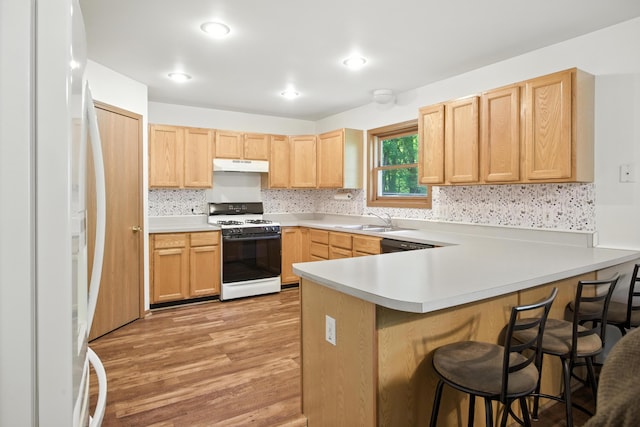 26434 King Rd, Romulus, MI 48174 - kitchen with white appliances, under cabinet range hood, light brown cabinetry, a peninsula, and a kitchen breakfast bar