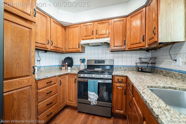 12141 Danforth Dr, Sterling Heights, MI 48312 - kitchen with stainless steel range with gas cooktop, under cabinet range hood, brown cabinetry, dark wood-style flooring, and backsplash