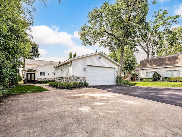 7660 Barnsbury Dr, West Bloomfield, MI 48324 - view of side of home with french doors, stone siding, a garage, driveway, and a yard