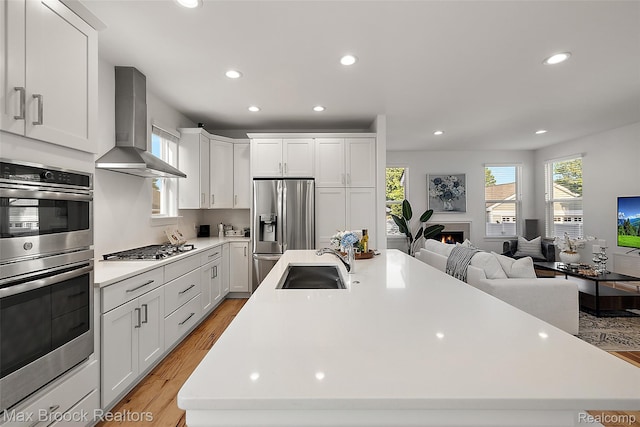 4260 Kent Rd, Royal Oak, MI 48073 - kitchen featuring wall chimney range hood, appliances with stainless steel finishes, an island with sink, recessed lighting, and light wood-type flooring