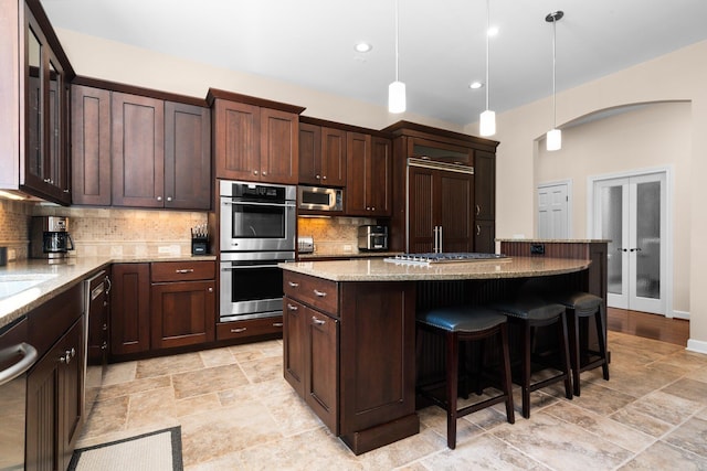 1303 Towsley Ln, Ann Arbor, MI 48105 - kitchen with appliances with stainless steel finishes, tasteful backsplash, a breakfast bar, light stone counters, and dark brown cabinetry