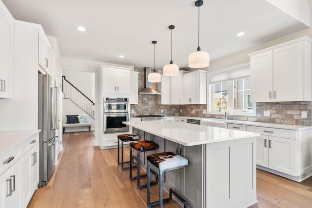 3078 N Spurway Dr, Ann Arbor, MI 48105 - kitchen featuring wall chimney exhaust hood, stainless steel appliances, a breakfast bar, light countertops, and recessed lighting