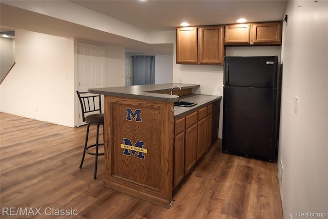 5280 Weston Ct, Commerce Twp, MI 48382 - kitchen with freestanding refrigerator, dark wood-style floors, dark countertops, brown cabinetry, and a breakfast bar