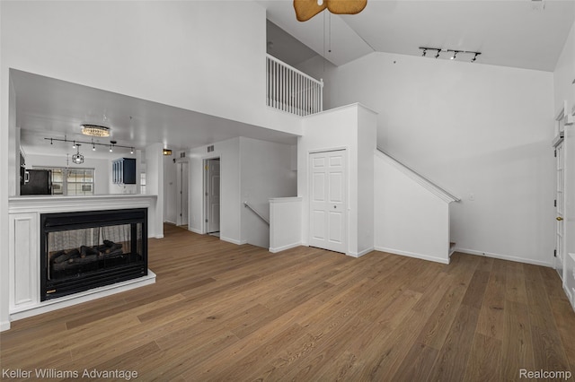 438 Old Pine Way, Walled Lake, MI 48390 - unfurnished living room featuring rail lighting, wood finished floors, a ceiling fan, high vaulted ceiling, and a multi sided fireplace