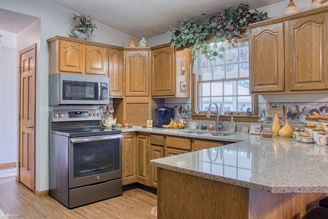 845 Riverlane Dr, Owosso, MI 48867 - kitchen with appliances with stainless steel finishes, a peninsula, light wood-style floors, vaulted ceiling, and light stone countertops