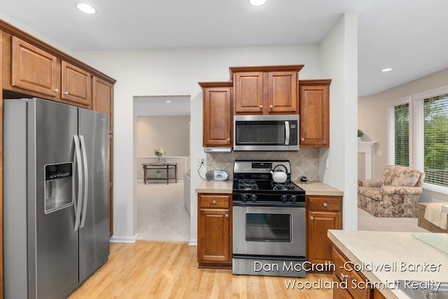1809 Woodside Trl NW, Grand Rapids, MI 49504 - kitchen with appliances with stainless steel finishes, light countertops, light wood-style flooring, brown cabinetry, and tasteful backsplash