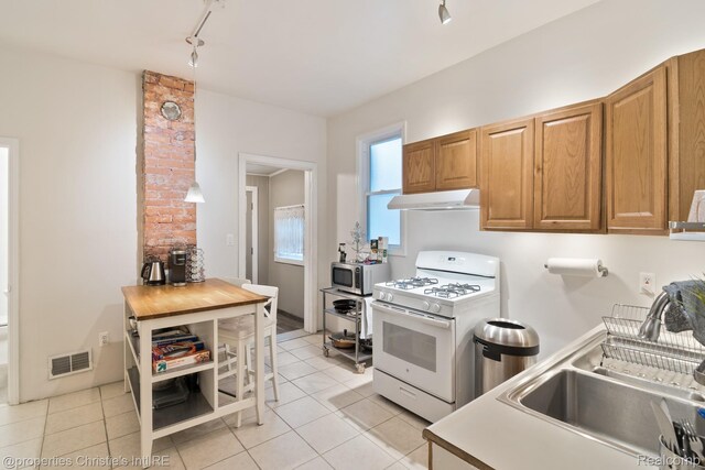 4751 Trumbull St, Detroit, MI 48208 - kitchen with white range with gas stovetop, under cabinet range hood, stainless steel microwave, track lighting, and light tile patterned flooring