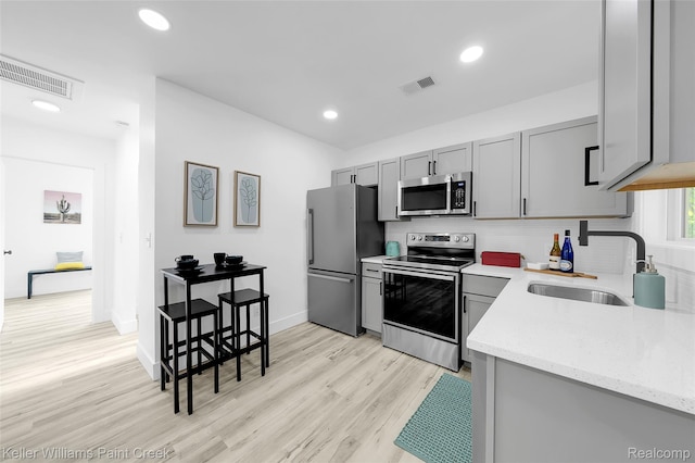 1641 Silman St, Ferndale, MI 48220 - kitchen with appliances with stainless steel finishes, gray cabinetry, light wood finished floors, light stone counters, and backsplash