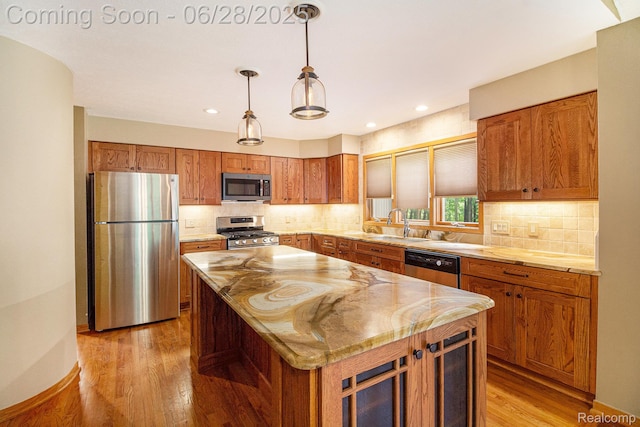 6375 Perryville Rd, Holly, MI 48442 - kitchen featuring stainless steel appliances, light wood finished floors, brown cabinetry, a kitchen island, and pendant lighting