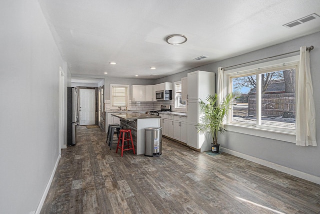 9922 S Sprinkle Rd, Portage, MI 49002 - kitchen with stainless steel appliances, a kitchen bar, dark wood-style floors, a kitchen island, and white cabinets
