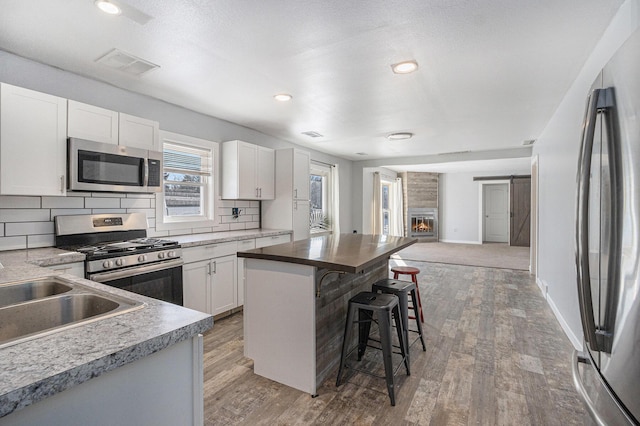 9922 S Sprinkle Rd, Portage, MI 49002 - kitchen featuring appliances with stainless steel finishes, a kitchen breakfast bar, open floor plan, tasteful backsplash, and white cabinets