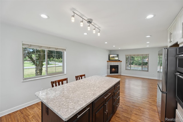 3395 W Maple Rd, Wixom, MI 48393 - kitchen featuring light countertops, a center island, light wood-type flooring, a tiled fireplace, and freestanding refrigerator